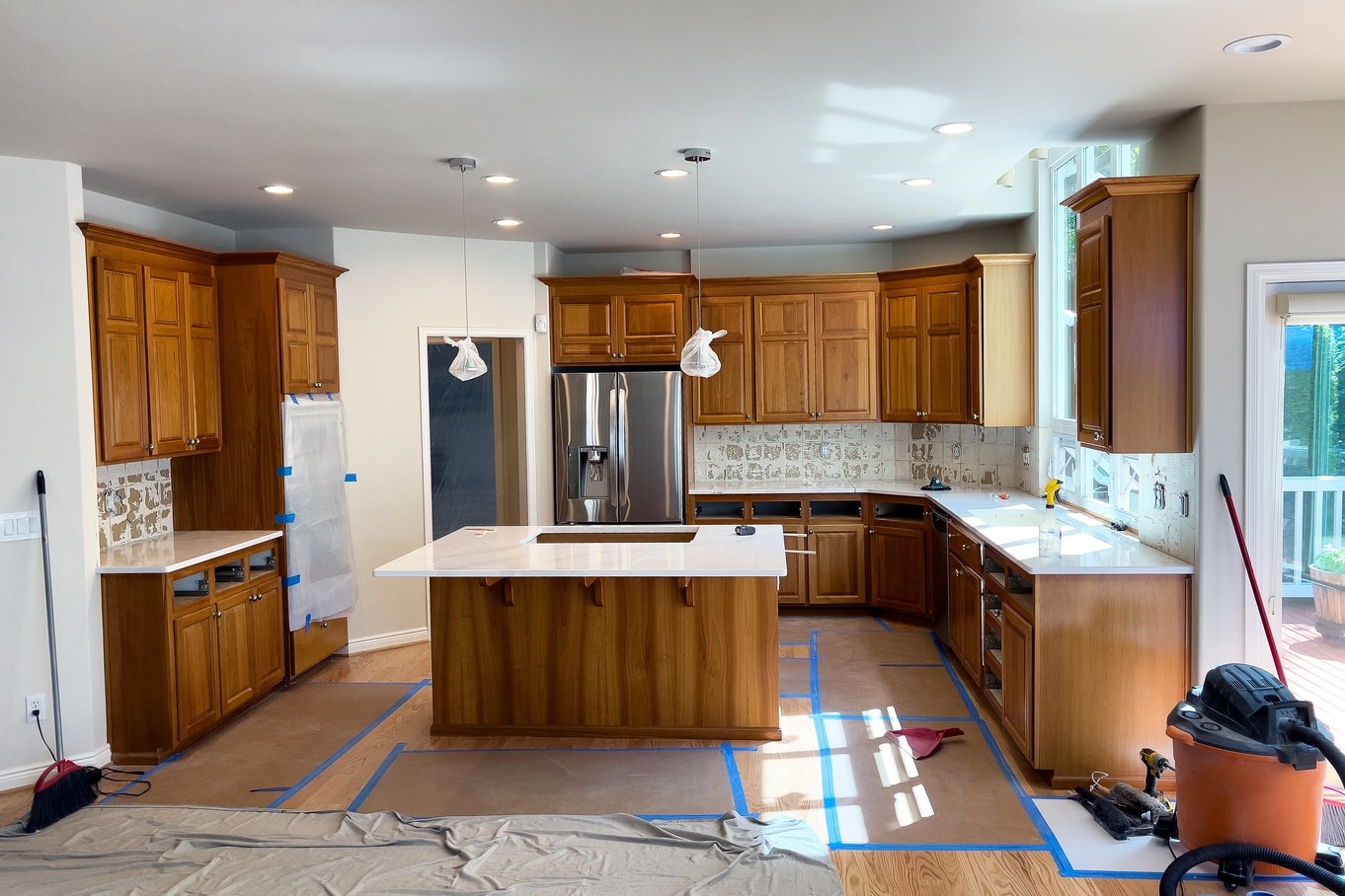 A home kitchen under renovation with quartz countertops, dark wood cabinetry, and coverings to protect materials.