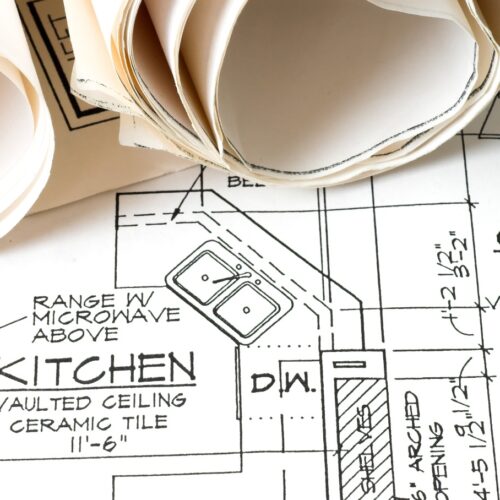 home improvement contractors Close-up of rolled blueprints over a residential floor plan labeled kitchen, with appliance locations and measurements.