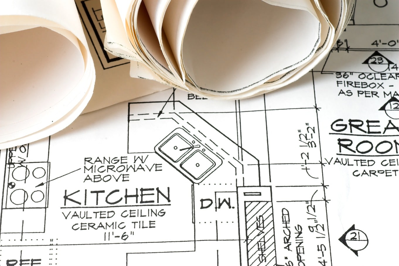 Close-up of rolled blueprints over a residential floor plan labeled kitchen, with appliance locations and measurements.
