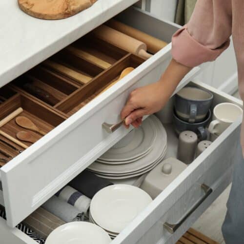 home improvement contractors A man is standing by an open drawer. Inside the drawer is plates and other kitchen utensils.