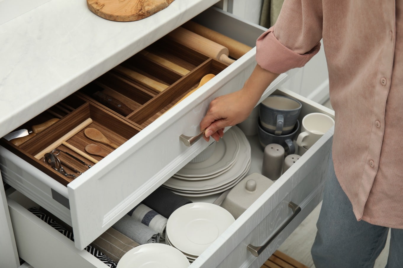 A man is standing by an open drawer. Inside the drawer is plates and other kitchen utensils.