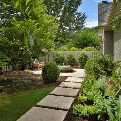 home improvement contractors A backyard with a stone path leading to a patio that is shrouded with green trees. There is a fence around the yard.