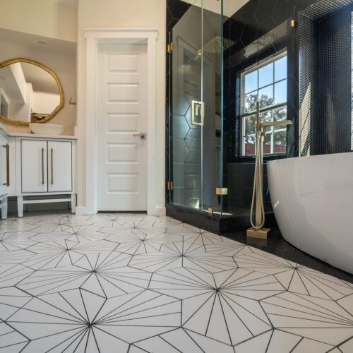 home improvement contractors A white bathtub beside a black tiled glass shower in a bathroom with geometric floor tiles and a white vanity.