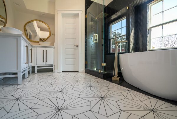 A white bathtub beside a black tiled glass shower in a bathroom with geometric floor tiles and a white vanity.