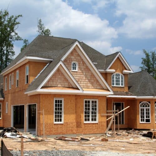 home improvement contractors Two-story house under construction with exposed wood sheathing, a shingled roof, and building materials scattered across the yard.