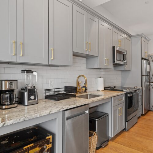 home improvement contractors A modern galley kitchen with grey cabinets, gold hardware, stainless-steel appliances, wooden floors, and white walls.