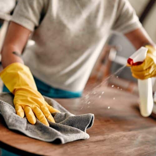 home improvement contractors A woman is wearing yellow gloves as she uses a spray bottle and cleaning rag to clean a tabletop.